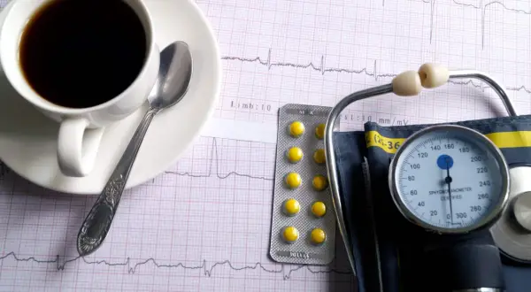 Kawa, tabletki i ciśnieniomierz na tle EKG. Czy kawa podnosi ciśnienie?