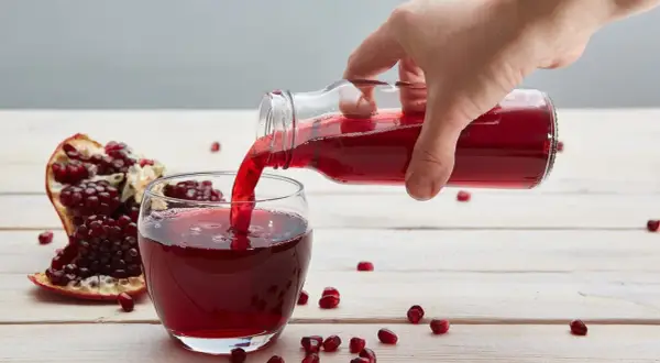 Ręka nalewa sok z granatu do szklanki. Obok leży połówka owocu. Ile pić dziennie?