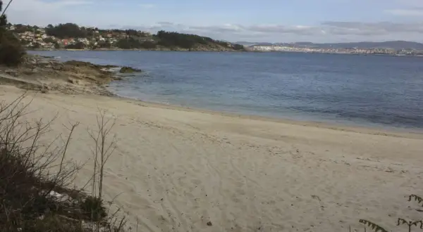 Arena dorada en la playa temperans, con el mar azul y una ciudad al fondo.