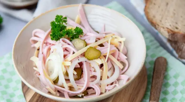 Ein köstlicher schweizer Wurstsalat mit Gurken, Zwiebeln und Käse, garniert mit Petersilie.