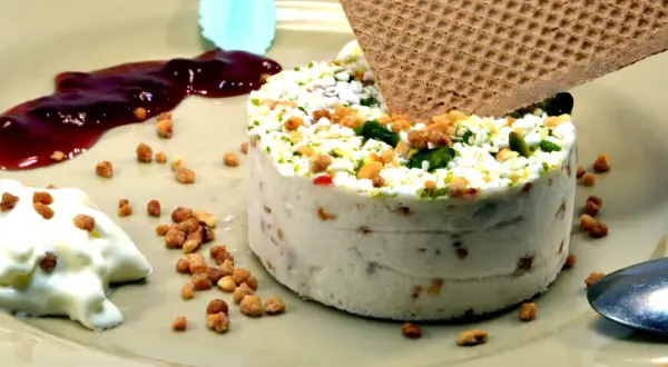 Un délicieux nougat glacé, parsemé de fruits secs et de pistaches, servi avec un coulis de fruits rouges et une touche de crème.