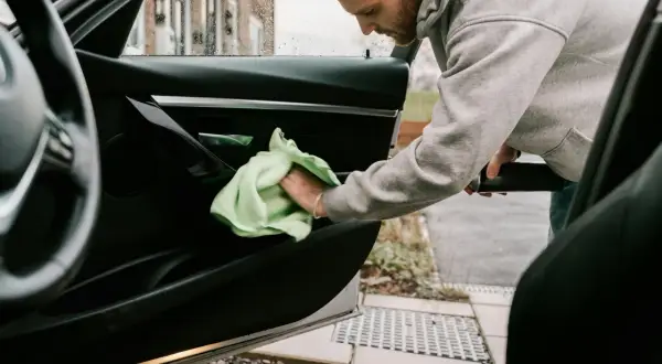 Man rengör bilens dörrpanel med en grön trasa. En fräsch doft i bilens interiör är målet.