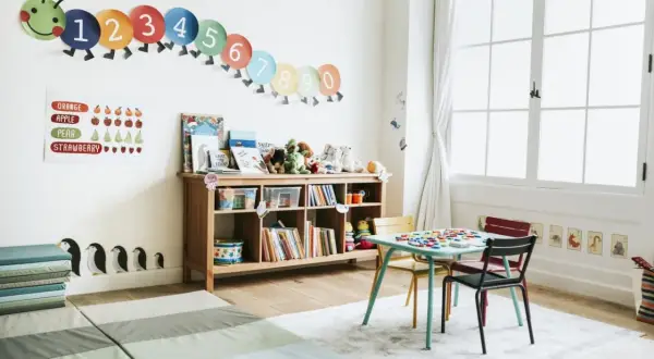 A bright, organized playroom with a number caterpillar, fruit chart, books, toys, and a small table and chairs, perfect for learning and play.