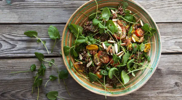 En härlig quinoa sallad med körsbärstomater, gröna blad och mandelspån, serverad i en vacker skål på en träbakgrund.