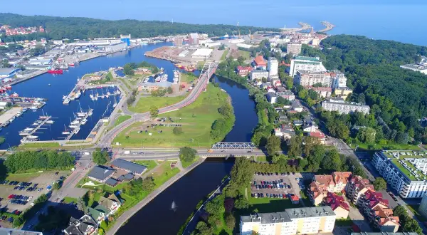 Widok z lotu ptaka na port i rzekę w Kołobrzegu. Widoczne liczne jachty, mosty, budynki mieszkalne i tereny zielone. Kołobrzeg atrakcje turystyczne w pełnej krasie.