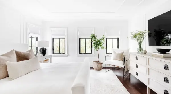 A serene, feminine black and white bedroom with a plush white bed, textured pillows, and a black lamp.