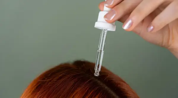 Dłoń z pipetką aplikuje serum na skórę głowy. Idealne rozwiązanie, czym nawilżyć skórę głowy i zadbać o włosy.