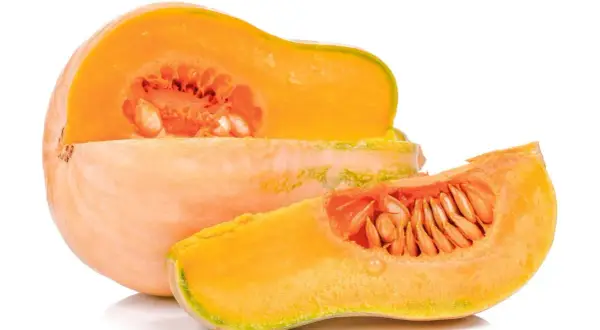 Pomarańczowa dynia, przekrojona na pół, z widocznymi nasionami. Obok leży plasterek tej samej odmiany dyni.
