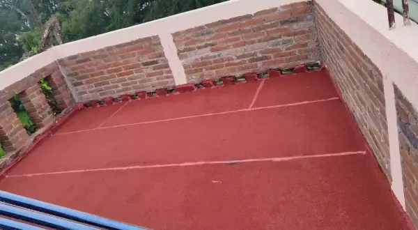 Terraza con pintura impermeabilizante roja recién aplicada. Se aprecian ladrillos y tubos de calentador solar.