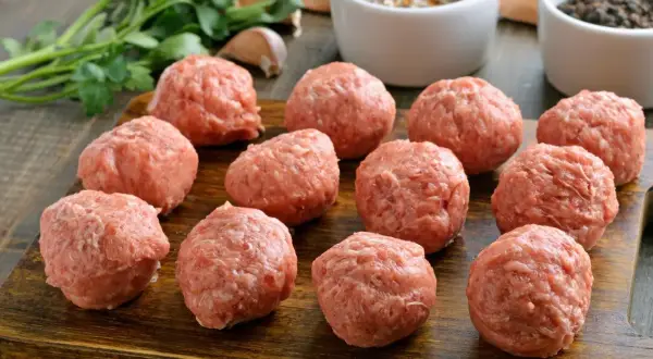 Gotowe do smażenia, obłędne kotlety mielone. Na drewnianej desce leży kilkanaście okrągłych porcji mięsa mielonego, obok pęczek natki pietruszki i czosnek.