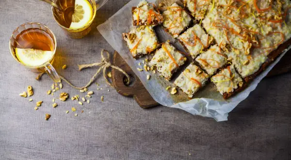 En härlig vegansk morotskaka med glasyr, nötter och citrusskal. Två koppar te med citron står bredvid.