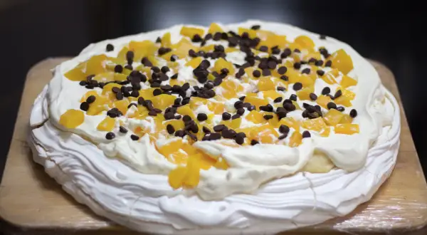 En härlig anna pavlova tårta med vispgrädde, persikobitar och chokladknappar.