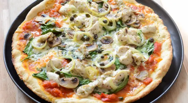Pyszna pizza z kurczakiem, pieczarkami i szpinakiem, polana sosem pomidorowym.