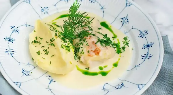 En vacker tallrik med torskrygg recept, serverad med krämigt potatismos och en grön dillolja.