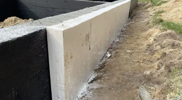 Izolacja ze styropianu na czarnej ścianie fundamentowej. To dobry sposób, co położyć na fundament domu, by zapewnić mu ciepło.