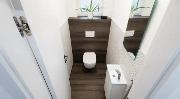 Bagno piccolo con WC sospeso, lavandino bianco e specchio asimmetrico. Un esempio di come piastrellare un bagno piccolo con stile.
