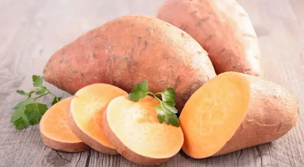 Patates douces entières et tranchées, garnies de persil frais, sur fond de bois. Un délice orangé prêt à être cuisiné.