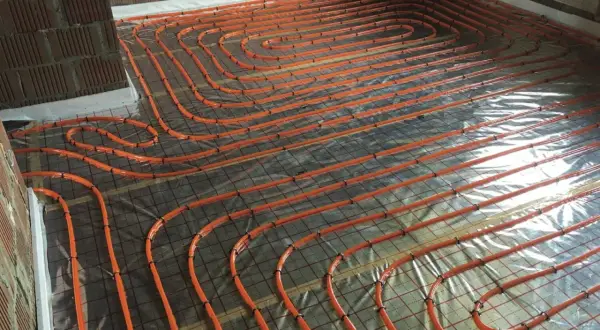 Pomarańczowe rury ogrzewania podłogowego ułożone na folii, przygotowane do wylania betonu. To kluczowy etap hydroizolacji chudziaka.