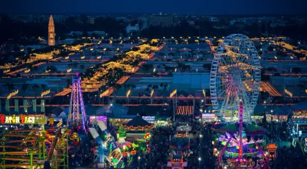 Nocne, rozświetlone atrakcjami wesołego miasteczka, gdzie trwa **feria de abril**. Widać diabelski młyn, kolejki górskie i tłumy ludzi.