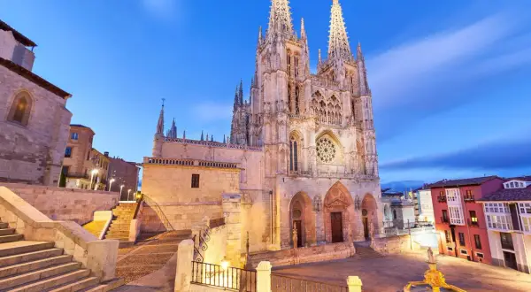 Majestuosa catedral de Burgos al anochecer, con sus agujas góticas iluminadas y el cielo azul crepuscular.
