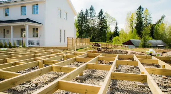 Grundarbete för att bygga altan på mark. Träkonstruktionen är på plats framför ett vitt hus.