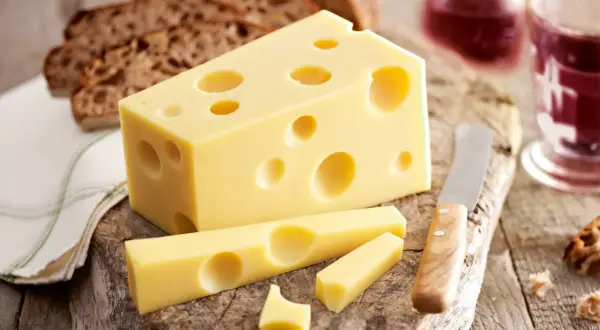Ein Stück Emmentaler mit seinen charakteristischen Löchern, daneben Brot und ein Glas Rotwein. Die Herkunft des Käses ist unverkennbar.