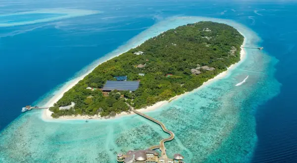 Soneva Fushi: üppige Insel mit Villen, Solaranlagen und einem Steg zu einem Restaurant im türkisfarbenen Wasser.