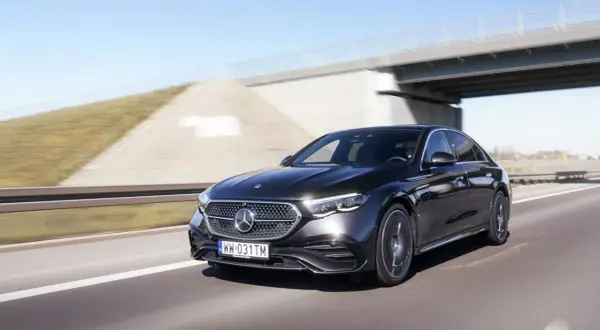 Czarny Mercedes E220d pędzi autostradą pod mostem.