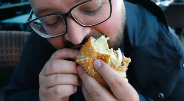 Mężczyzna w okularach je dużego burgera.