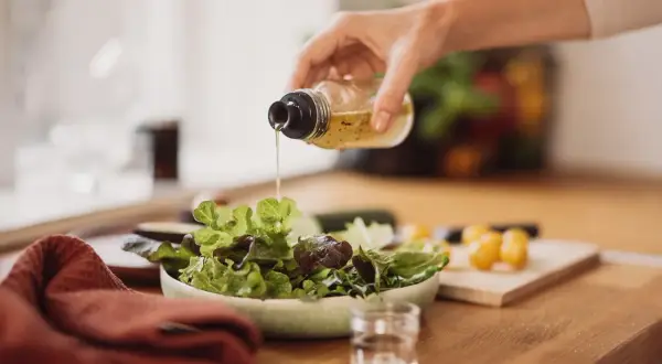 Frische Salatblätter werden mit einem Dressing beträufelt. Rotweinessig ist eine gesunde Wahl, besonders in der Schwangerschaft.