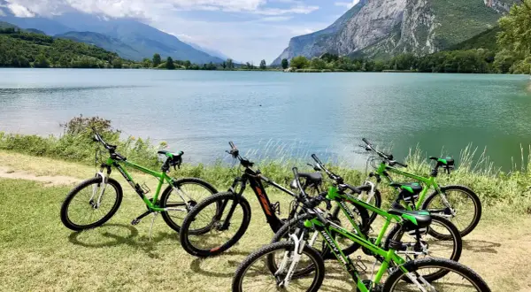 Biciclette verdi pronte per un'avventura sul lungolago di Riva del Garda, con montagne maestose sullo sfondo.