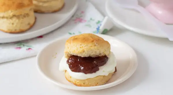 Un delicioso scone de reposteria inglesa, cubierto con crema y mermelada, listo para disfrutar.