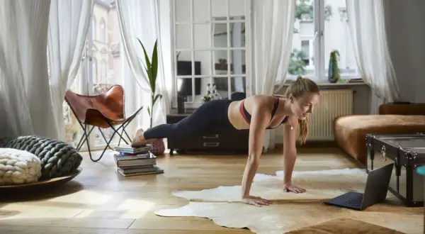 Femme en position de planche, suivant un entraînement de 7 minutes sur son ordinateur portable dans un salon lumineux.