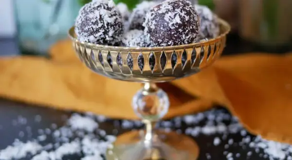 Nyttiga chokladbollar rullade i kokosflingor, serverade i en vacker guldfärgad skål. En perfekt, hälsosam godsak!