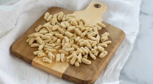 Un mucchio di cavatelli pugliesi freschi su un tagliere di legno, pronti per essere cucinati.