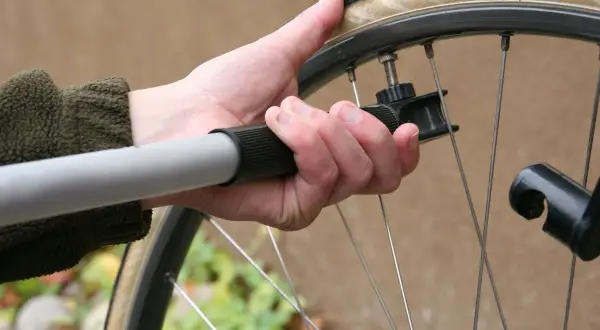Ręka trzyma pompkę rowerową, gotową do sprawdzenia ciśnienia w oponach.