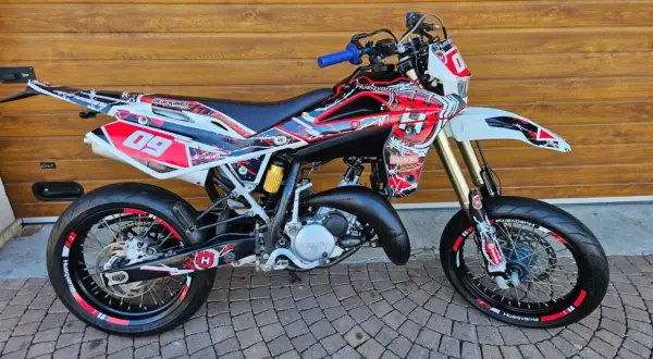 Husqvarna TE 125 z agresywnym oklejeniem w czerwono-białe wzory, gotowa do jazdy po torze.