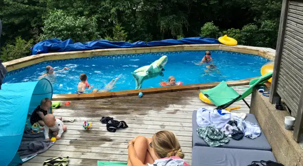 Barn njuter av en solig dag vid poolen, med en uppblåsbar haj och flytleksaker. En bebis leker i ett tält på altanen, perfekt för spf barn.