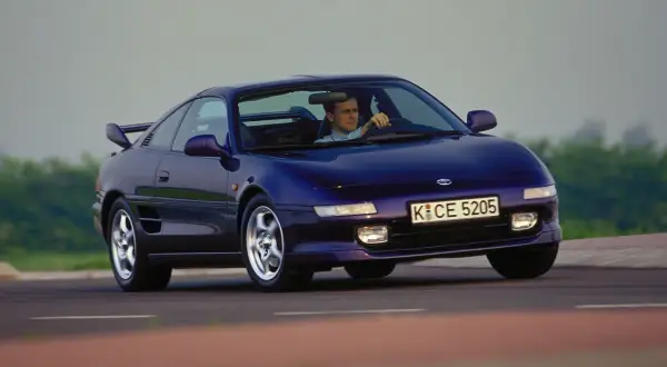 Mężczyzna prowadzi fioletowe Toyota MR2 SW20 po krętej drodze.