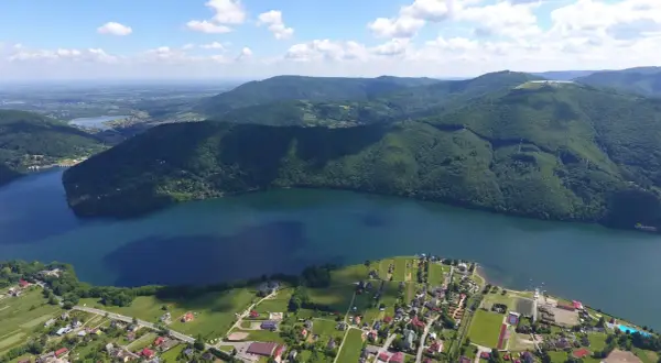 Malownicze krajobrazy i jezioro w Międzybrodziu Bialskim. Widać zabudowania, pola i zalesione wzgórza, idealne na wypoczynek i odkrywanie atrakcji.
