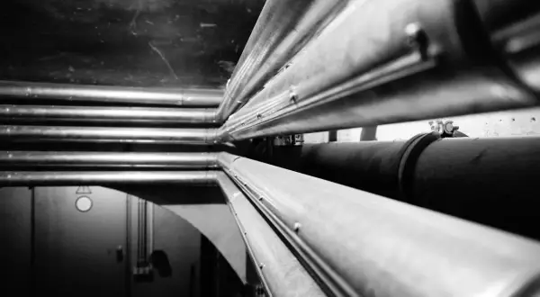 Mehrere Heizungsrohre werden in einem dunklen Raum verlegt. Sie verlaufen parallel und bilden ein komplexes Netzwerk.