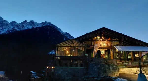 Rifugio alpino illuminato con una stella di Natale, circondato da montagne innevate. I forni di sopra sono spenti, ma l'atmosfera è calda e accogliente.
