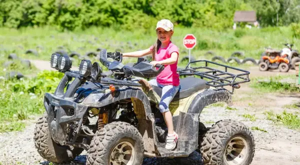 Uśmiechnięta dziewczynka w czapce siedzi na quadzie, gotowa na przygodę. To idealne miejsce dla miłośników adrenaliny, kategoria B1.