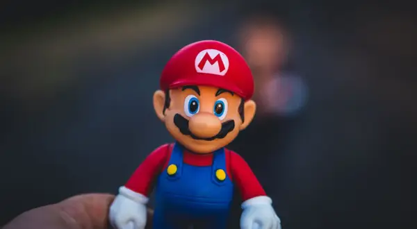 Figurka Mario w czerwonej czapce z literą M i niebieskich ogrodniczkach, trzymana na dłoni.