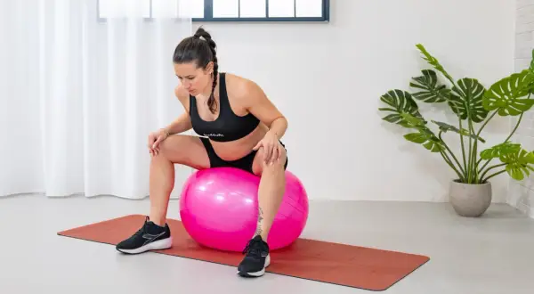 Mujer embarazada sentada en una pelota de ejercicio rosa, preparándose para fortalecer el suelo pélvico.