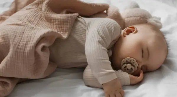 Dolce neonato di 3 mesi dorme sereno, avvolto in una copertina color pesca, con un ciuccio in bocca.