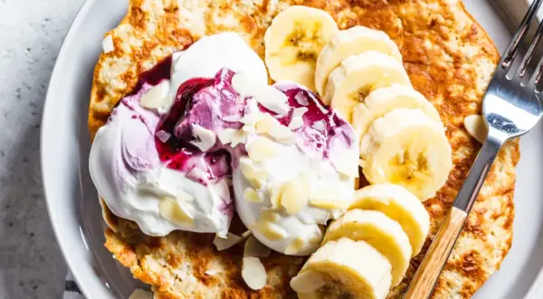 Puszysty omlet z bananem, udekorowany bitą śmietaną, musem jagodowym i płatkami migdałów. Idealne śniadanie.