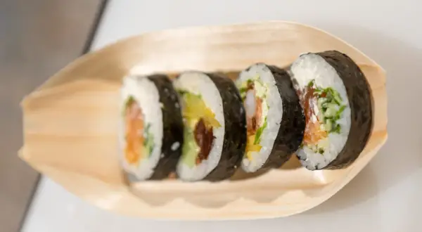 Pięć kawałków sushi z łososiem, awokado i krewetkami na drewnianej łódce. Różne rodzaje sushi nazwy w zasięgu ręki.