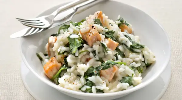 Un crémeux risotto épinard avec des morceaux de saumon. Un plat savoureux et coloré, prêt à être dégusté avec une fourchette et un couteau.