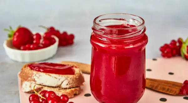 Glas mit Erdbeer Johannisbeer Marmelade, daneben Brot mit Marmelade und frische Beeren.
